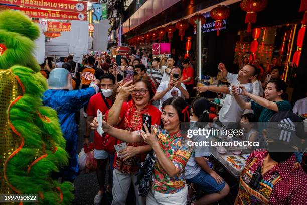 Tourists cheer and take photos as a lion dance troupe performs on Lunar New Years Eve on February 09, 2024 in Bangkok, Thailand. The Chinese diaspora...