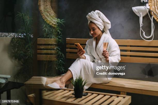 young woman in a bathrobe using a smartphone in a hotel spa - bathrobe stock pictures, royalty-free photos & images