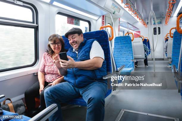 cheerful latin senior couple enjoying smart phone entertainment and social media during train travel. retirement escapade. - chilean people stock pictures, royalty-free photos & images