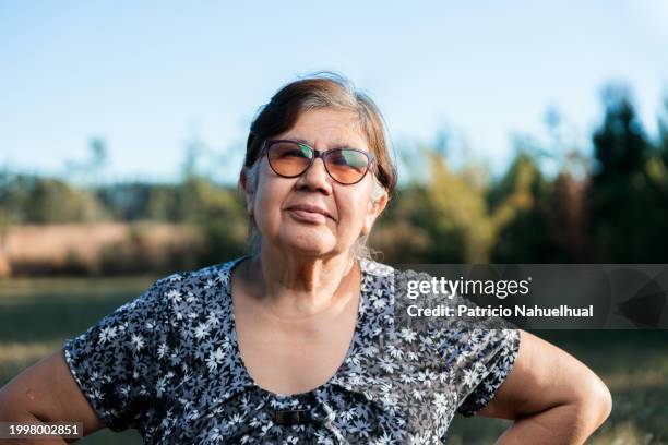 portrait of smiling latina senior woman standing on countryside and looking at camera. - front flash photography foto e immagini stock