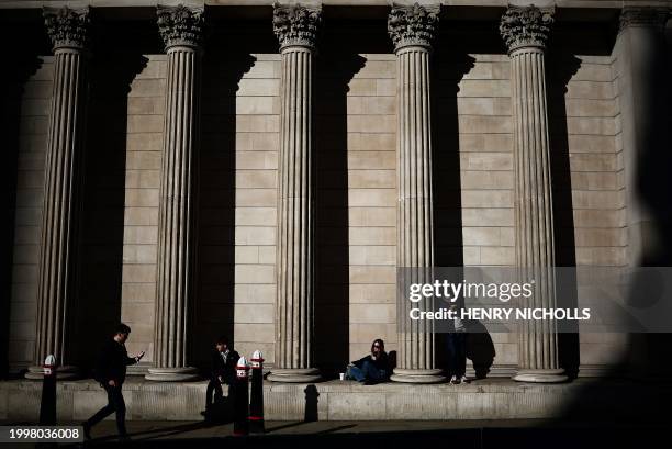 People sit in between the columns of The Bank of England as the building is illuminated by a ray of sunlight, in central London, on February 12, 2024.