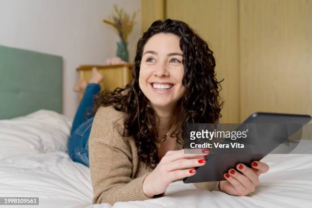 spanish woman smiling using technology at confortable bedroom - confortable imagens e fotografias de stock