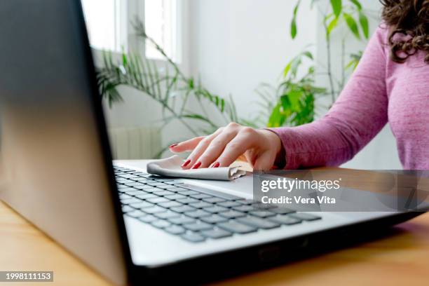 close up view of cropped woman hand using cleaning equipment to disinfect computer keyboard on top of wooden table - antiseptic wipe stockfoto's en -beelden