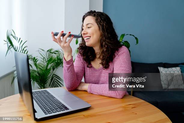 side portrait of beautiful spanish woman online chatting at blue living room with plants in background - vita domestica fotografías e imágenes de stock