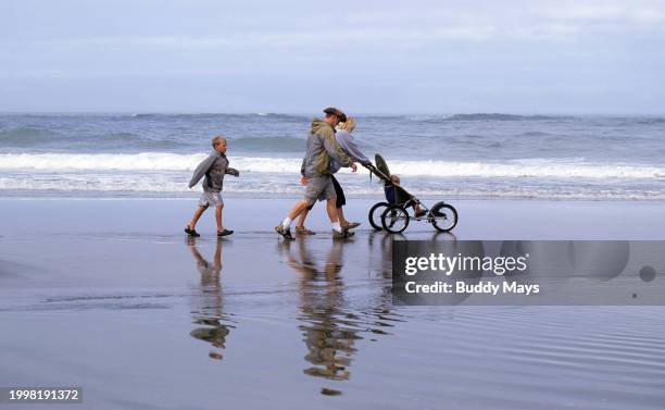 Family of visitors walks briskly along the Pacific Ocean beach in Lincoln City, Oregon, pushing their baby carriage on a breezy and foggy summer...