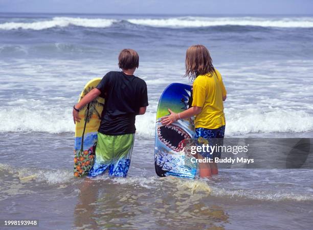 Two eleven-year-old girls with their boogie boards wait for the best waves in a rugged Pacific Ocean just off the beach in Lincoln City, Oregon,...