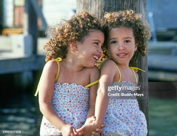 Two young African American identical twins sitting on a dock in the sun while their parents fish, on Padre Island, Texas, 1982. .