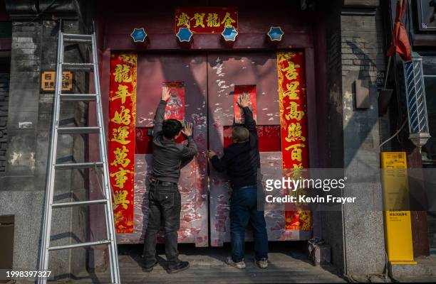 Men place posters of door gods, or Menshen, for the Chinese New Year and Spring Festival on a door of a traditional courtyard on February 9, 2024 in...