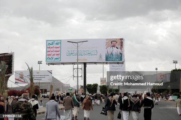 Yemen's Houthi followers walk under a billboard depicting the picture of the Houthi movement founder Husein Badr Al-Deen Al-Houthi, established on a...