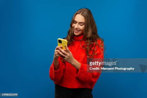 smiling young emotional girl looking at the screen using smart phone in blue background - cut out dress foto e immagini stock