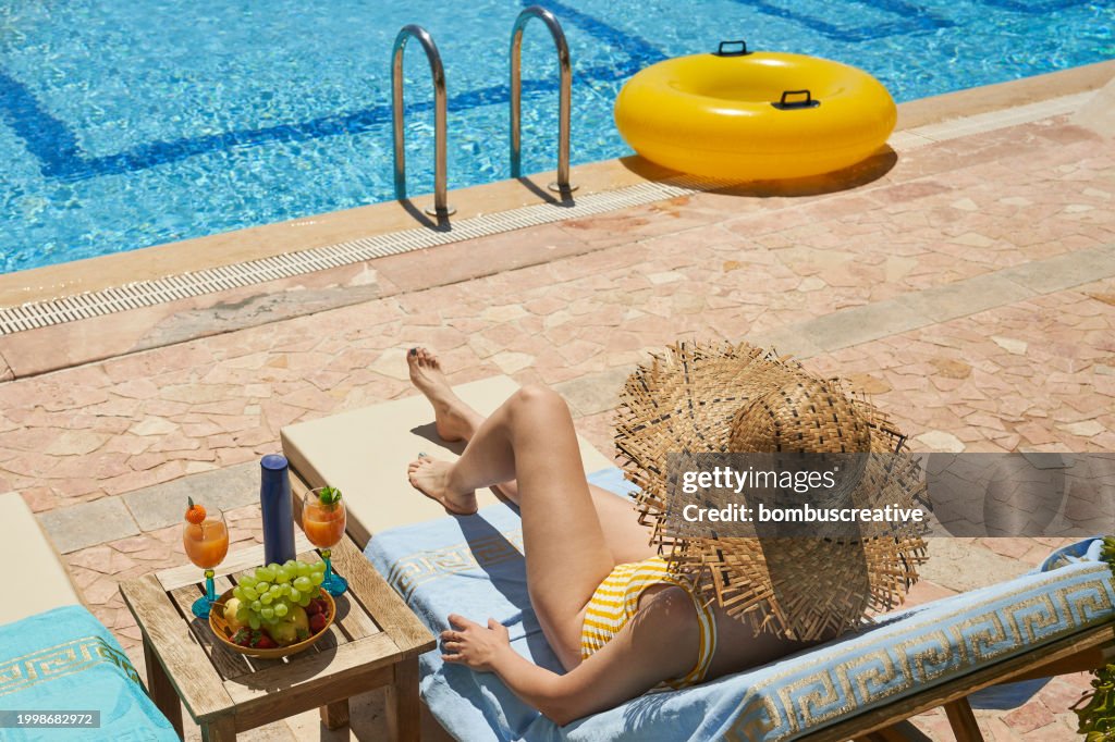 Fashionable woman sitting by the pool on the empty deck