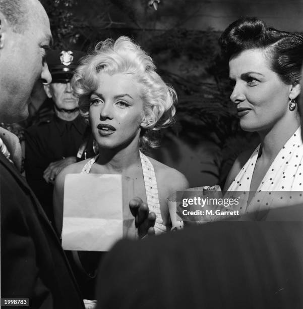 American actresses Marilyn Monroe and Jane Russell speak to an unidentified man as they promote director Howard Hawks' film, 'Gentlemen Prefer...