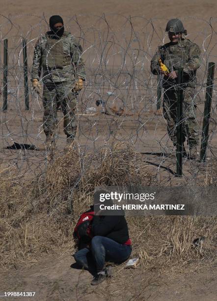 Texas National Guard agent plays with a toy rubber chicken that makes sounds, in front of an immigrant, near a barbed wire fence installed to prevent...