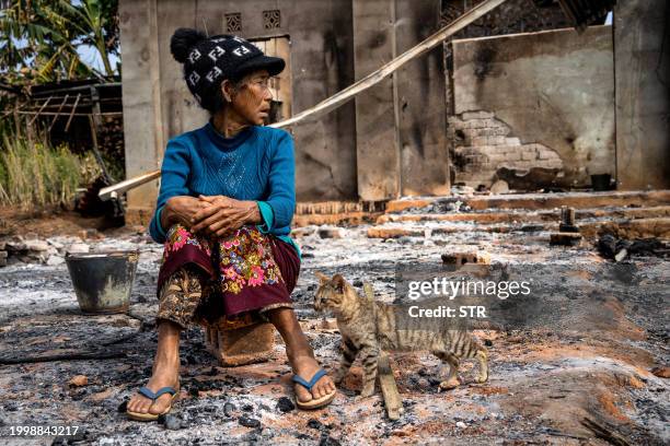 This photo taken on February 4, 2024 shows a woman sitting next to a cat in front of her house damaged following fighting between Myanmar's Military...