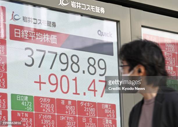 Pedestrian looks at a stock board in Tokyo showing the 225-issue Nikkei Stock Average rising more than 900 points from the previous day's close on...