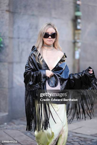 Guest wears sunglasses, a necklace, a beaded / embellished / rhinestones Coperni bag, a black leather jacket with fringes, a lustrous shiny silk slit...