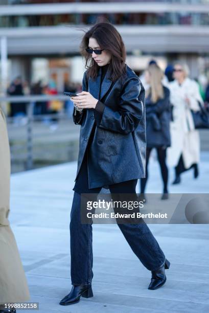 Guest wears sunglasses, a black turtleneck , a black leather oversized blazer jacket, black denim jeans pants , high heels pointed boots, outside...