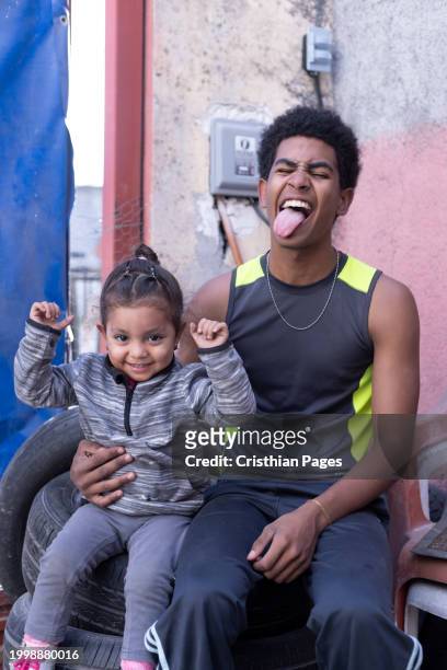 cuban teenager with afro hair sitting on tires, his sister born in mexico, 2 and a half years old, happy and enjoying - nuevo leon state stock pictures, royalty-free photos & images