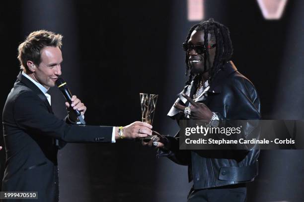 French rapper Gazo celebrates winning the Best Male Artist award next to Master of Ceremony French TV host Cyril Feraud during the 39th "Les...