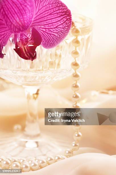 pearl jewelry and cocktail glass with delicate purple orchid flower on beige orange tulle fabric in peach color. - fuchsia orchids stock pictures, royalty-free photos & images