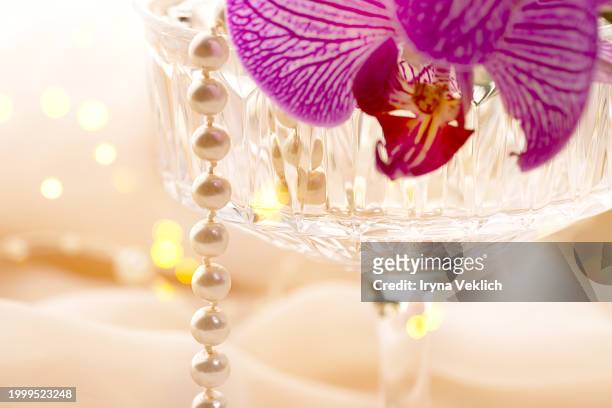 pearl jewelry and cocktail glass with delicate purple orchid flower on beige orange tulle fabric in peach color. - fuchsia orchids stock pictures, royalty-free photos & images