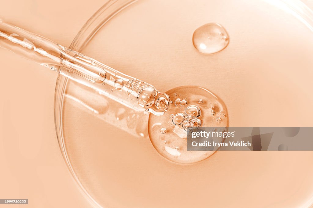 Glass Pipette with Face Serum or Essential Oil with Oxygen Aqua Bubbles and a drop of liquid in Petri Dish on a pastel beige orange background with shadow in peach color.