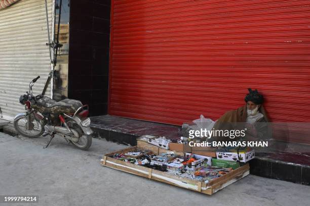 Man selling chargers and electrical items along a road with its shops closed waits for customers during a strike called by the Baloch Pashtun...