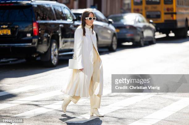 Guest wears white coat, beige pants, ankle boots, turtleneck, white sunglasses, bag outside Helmut Lang on February 09, 2024 in New York City.