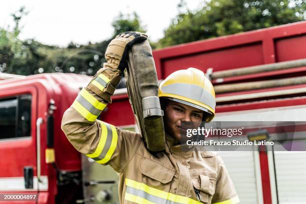 ritratto di un giovane vigile del fuoco che trasporta una manichetta antincendio all'aperto - operatore di prima linea foto e immagini stock
