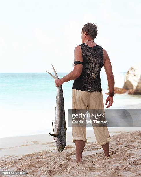 man on beach holding big fish, rear view - fish barbados stock pictures, royalty-free photos & images