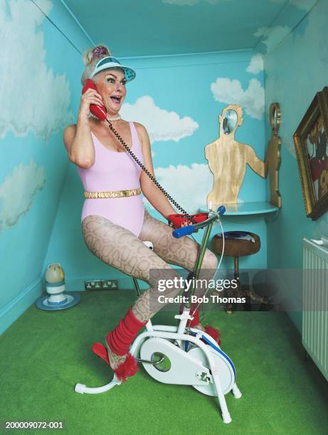 Mature woman on exercise bike, using telephone