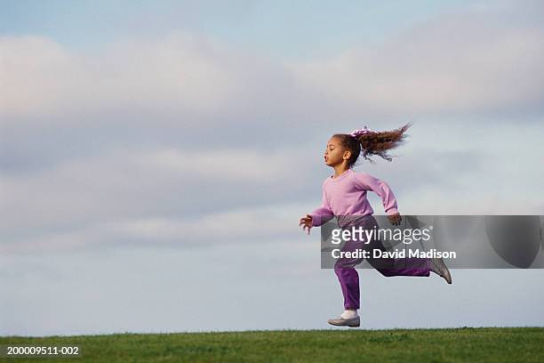 girl (4-6) running across field, side view - girl side view stockfoto's en -beelden