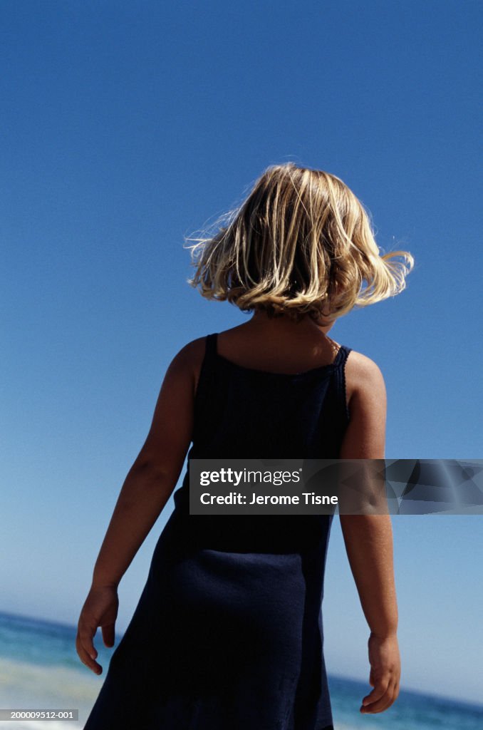 Girl (2-4) standing on beach facing ocean, rear view