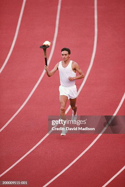 man running on track, carrying burning torch, elevated view - flaming torch stock pictures, royalty-free photos & images