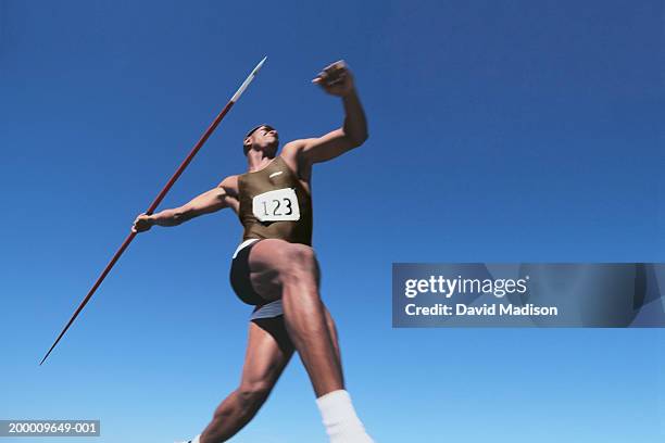 young male throwing javelin, low angle view (digital enhancement) - speerwurf stock-fotos und bilder