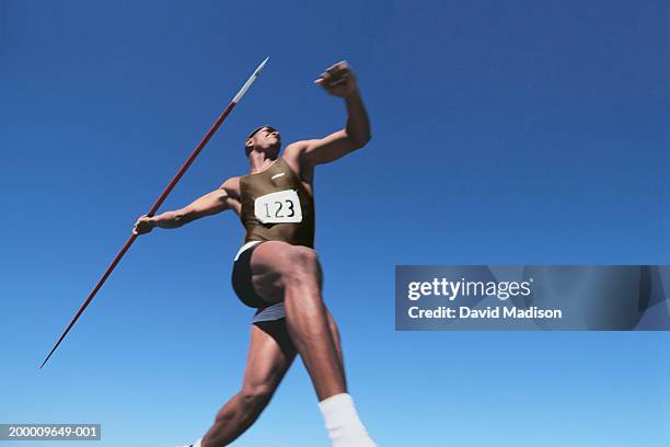young male throwing javelin, low angle view (digital enhancement) - jabalina fotografías e imágenes de stock
