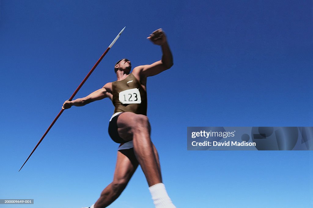 Young male throwing javelin, low angle view (digital enhancement)