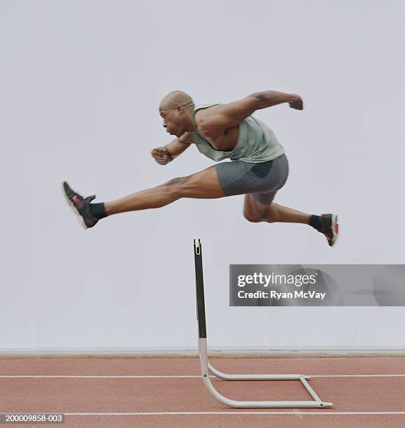 man jumping hurdle, side view - hordelopen atletiekonderdeel stockfoto's en -beelden