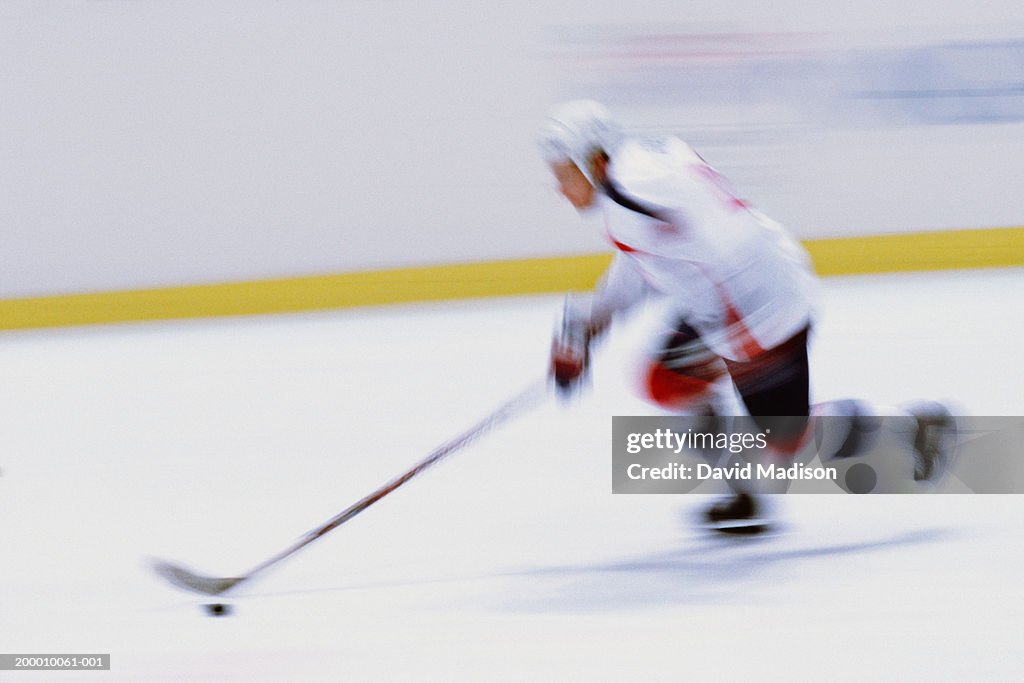 Ice hockey player skating with puck, side view (blurred motion)
