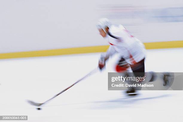 ice hockey player skating with puck, side view (blurred motion) - hockey puck stock pictures, royalty-free photos & images