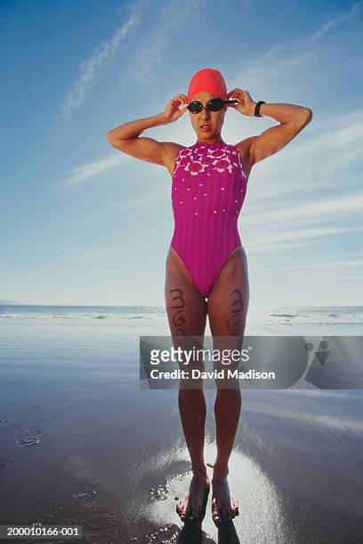 woman on beach preparing for swimming leg of triathlon - badeanzug stock-fotos und bilder