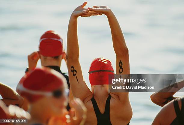 triathletes stretching before swimming leg of race (rear view) - race 8 stock pictures, royalty-free photos & images