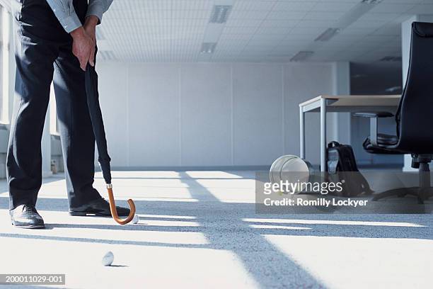 businessman practicing putting with umbrella, in office, low section - golf accessories stock pictures, royalty-free photos & images