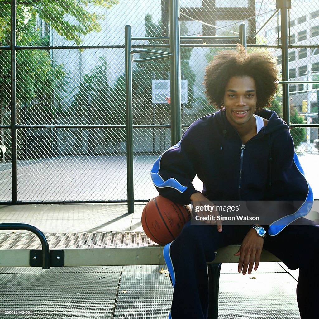 Young man sitting on bench with basketball, portrait