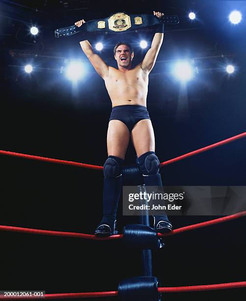 pro wrestler standing on ropes, holding championship belt - ringen stock-fotos und bilder