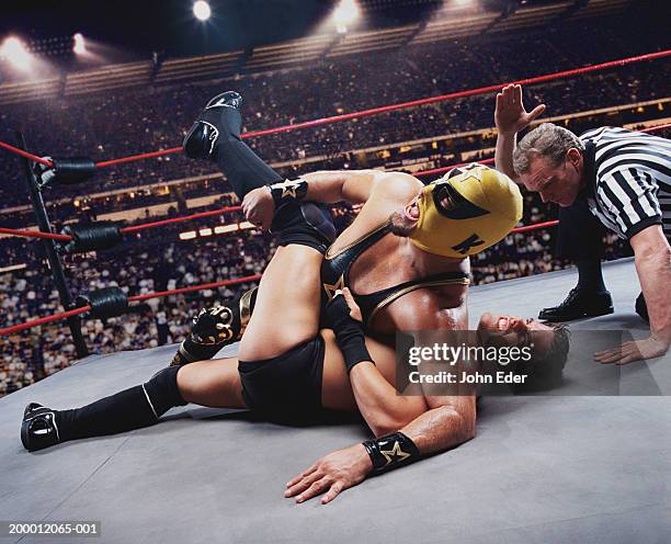 pro wrestler pinning opponent on mat, referee counting down - fuera de combate fotografías e imágenes de stock