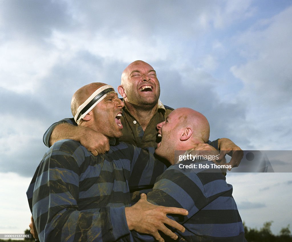 Three rugby players embracing and smiling