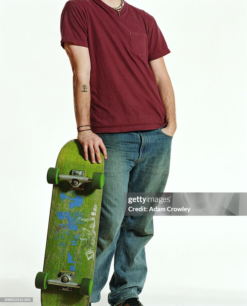 Young man holding skateboard, low section