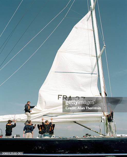 crew lowering sail on yacht - lowering photos et images de collection