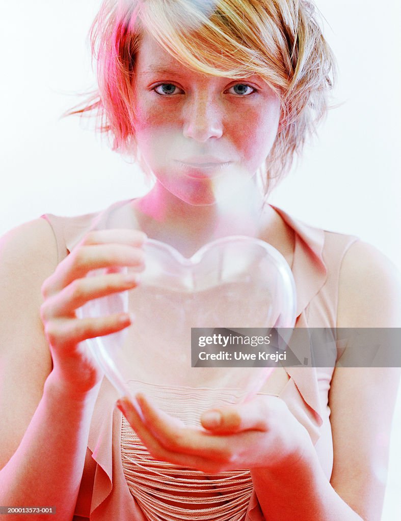 Young woman holding clear heart shaped ornament, portrait